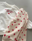 Weißes Sweatshirt mit rotem Print, kombiniert mit einer Hose mit Herzmuster.