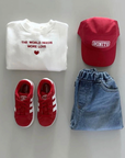 Outfit-Flatlay mit weißem Sweatshirt, roter Cap, Jeansrock und roten Sneakern.