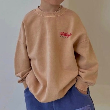 Kind trägt das beige „Frosted Flakes“ Sweatshirt – kleiner roter „Kellogg’s“ Print auf der Brust sichtbar.
