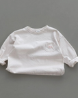Cremefarbenes Longsleeve-Tee mit Rundhalsausschnitt und kleinem Label auf der Brust.