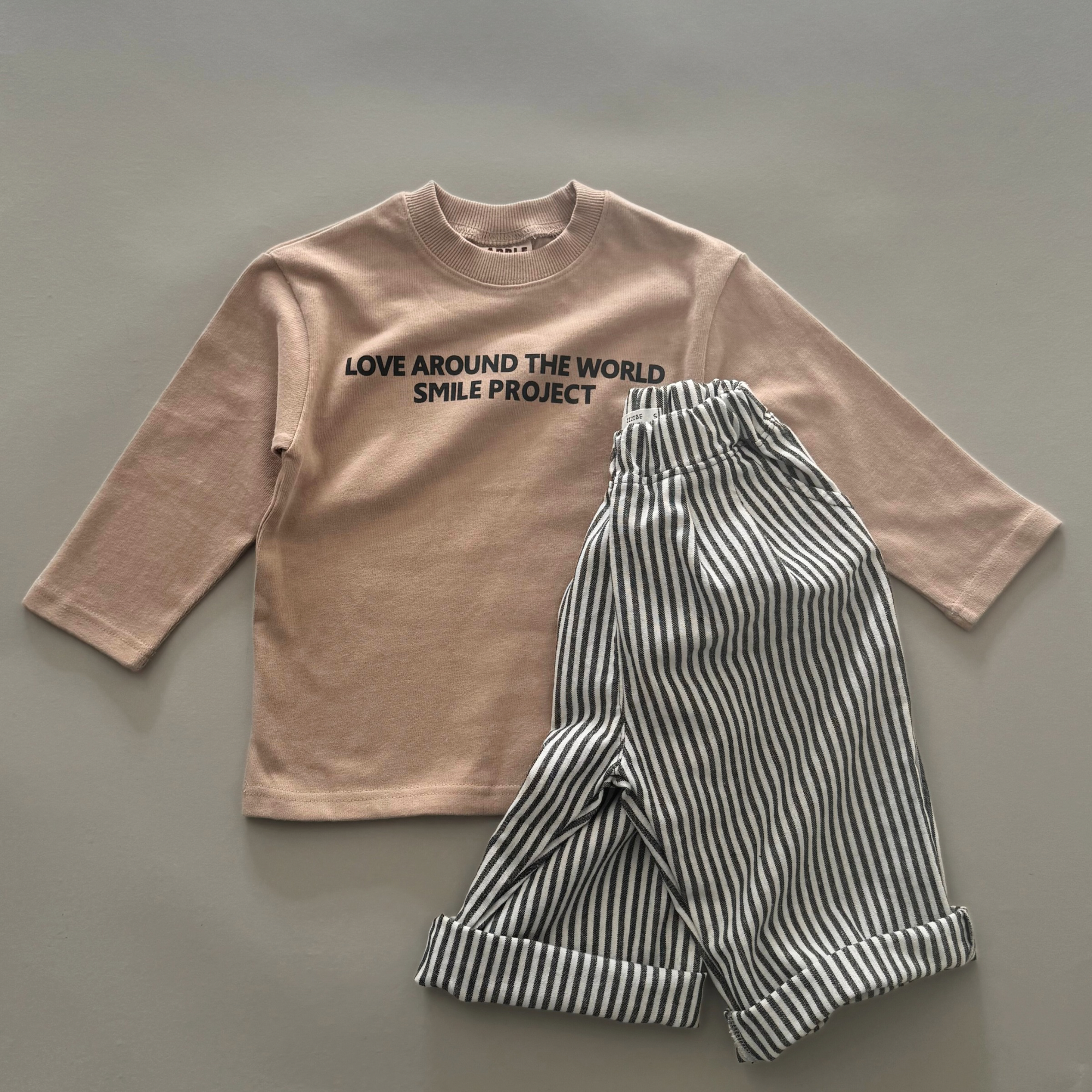 Beiges Longsleeve mit „LOVE AROUND THE WORLD“ Schriftzug, kombiniert mit einer schwarz-weiß gestreiften Hose.
