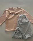 Beiges Longsleeve mit „LOVE AROUND THE WORLD“ Schriftzug, kombiniert mit einer schwarz-weiß gestreiften Hose.