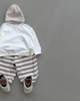 Ivoryfarbenes Longsleeve mit Boxy-Schnitt kombiniert mit gestreifter Hose und Schuhen und Beanie.