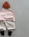 Roséfarbenes Boxy-Longsleeve kombiniert mit heller Mütze, beiger Hose und dunklen Schuhen.