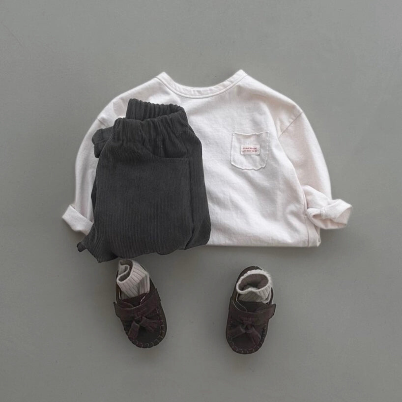 Cremefarbenes Longsleeve-Tee kombiniert mit dunkler Hose, grauer Cap und Sneakers.
