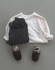Cremefarbenes Longsleeve-Tee kombiniert mit dunkler Hose, grauer Cap und Sneakers.