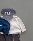 Cremefarbenes und dunkelblaues  Longsleeve-Tee kombiniert mit dunkler Hose, grauer Cap