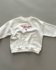 Weißes Sweatshirt mit rotem Schriftzug „THE WORLD NEEDS MORE LOVE“ auf der Vorderseite, Rundhalsausschnitt und gerippten Bündchen.