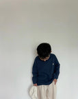 Kind trägt dunkelblaues Longsleeve mit beigefarbenen Hose
