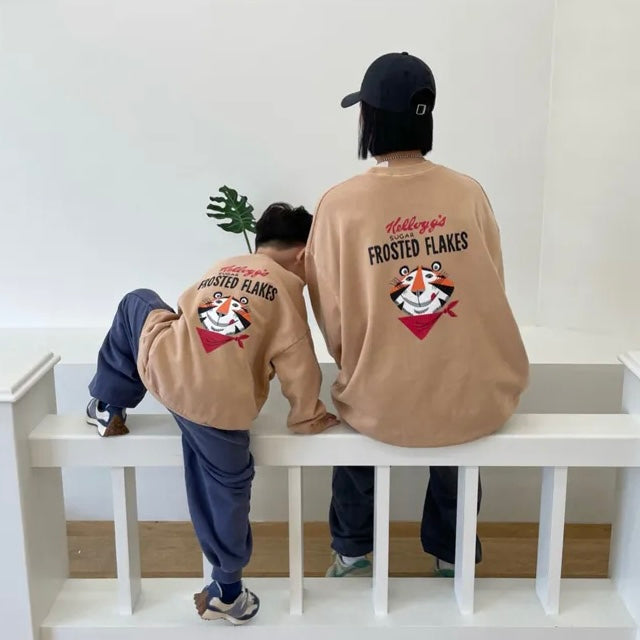 Kind und Erwachsener im beigen „Frosted Flakes“ Sweatshirt – großer Print mit Tony der Tiger auf dem Rücken.