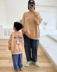 Spiegelbild von Kind und Erwachsenem im beigen „Frosted Flakes“ Sweatshirt – „Kellogg’s“ Schriftzug vorne, großer Print mit Tony der Tiger auf dem Rücken.