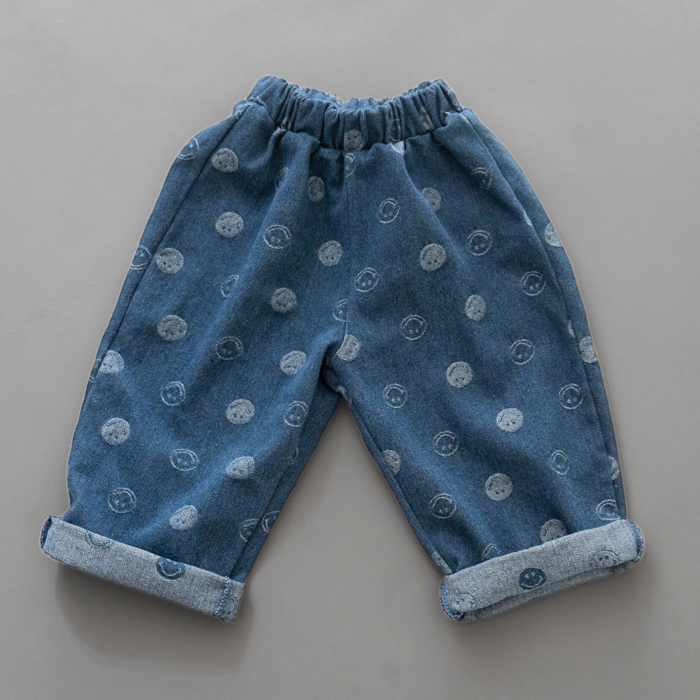 Blaue Denim-Hose mit Smiley-Prints – lockerer Schnitt, elastischer Bund und umgeschlagene Beinabschlüsse.