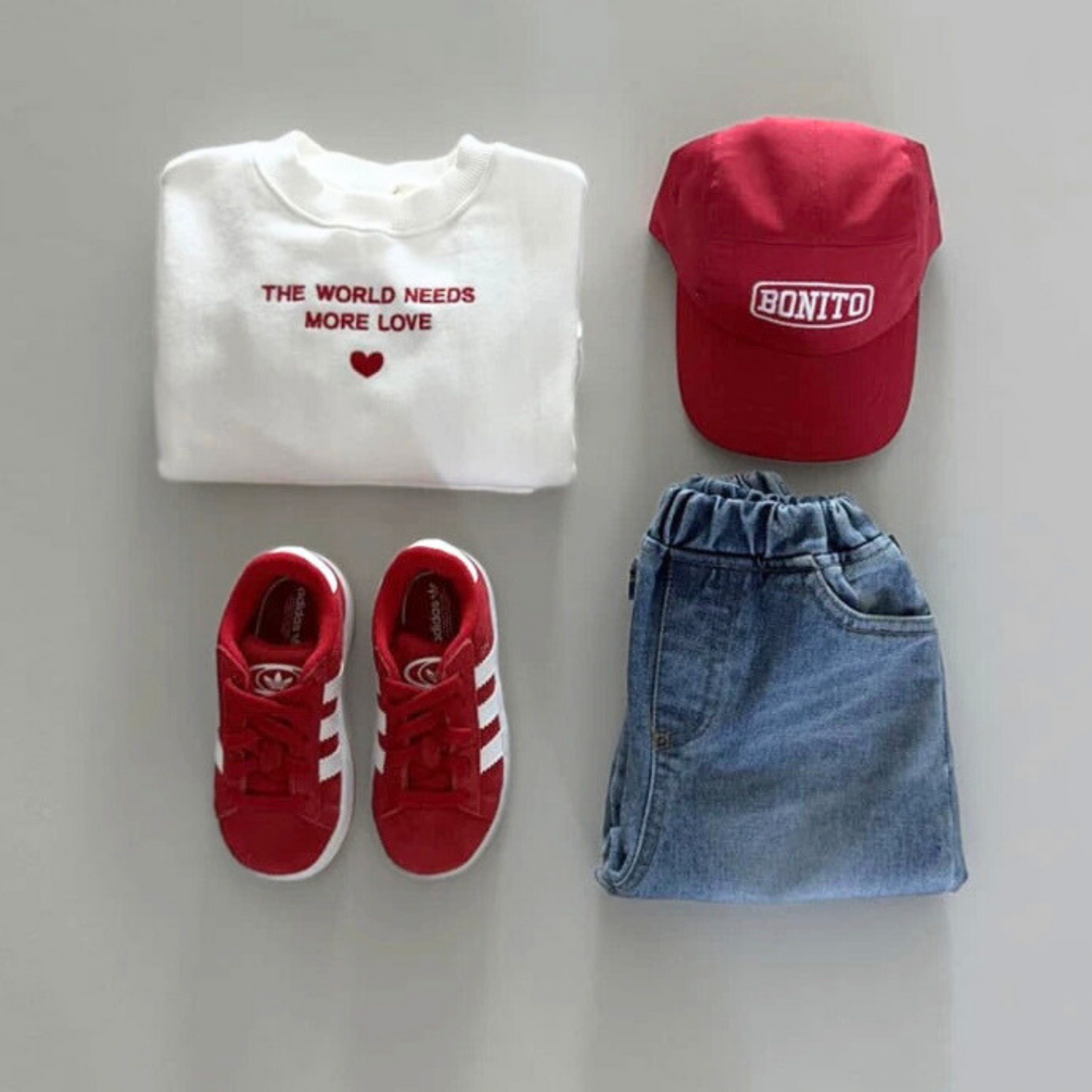 Outfit-Flatlay mit weißem Sweatshirt, roter Cap, Jeansrock und roten Sneakern.