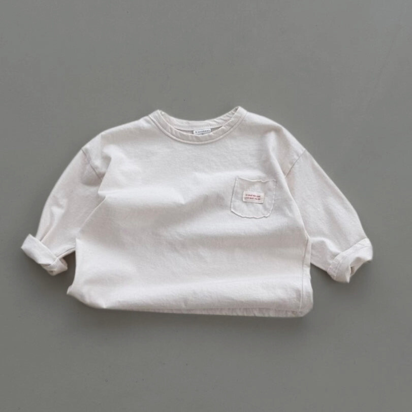 Cremefarbenes Longsleeve-Tee mit Rundhalsausschnitt und kleinem Label auf der Brust.