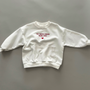 Weißes Sweatshirt mit rotem Schriftzug „THE WORLD NEEDS MORE LOVE“ auf der Vorderseite, Rundhalsausschnitt und gerippten Bündchen.