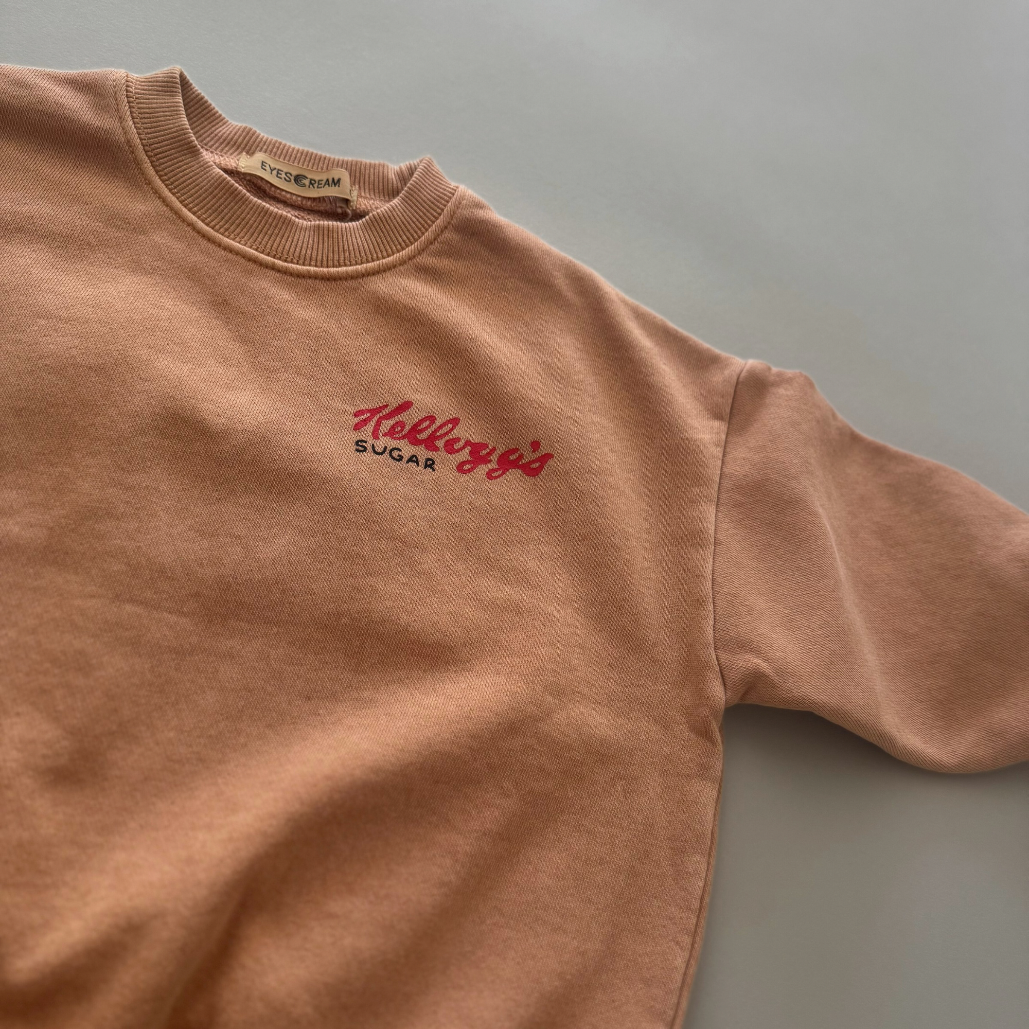 Kleiner roter „Kellogg’s“ Print auf der Brust des beigen Sweatshirts.