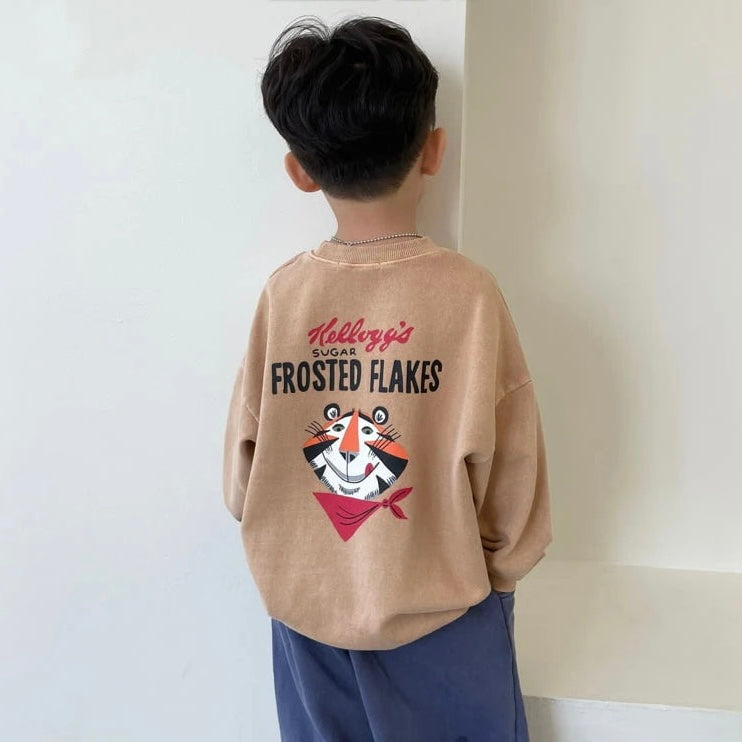 Kind trägt das beige „Frosted Flakes“ Sweatshirt – großer Tony der Tiger Print auf dem Rücken sichtbar.